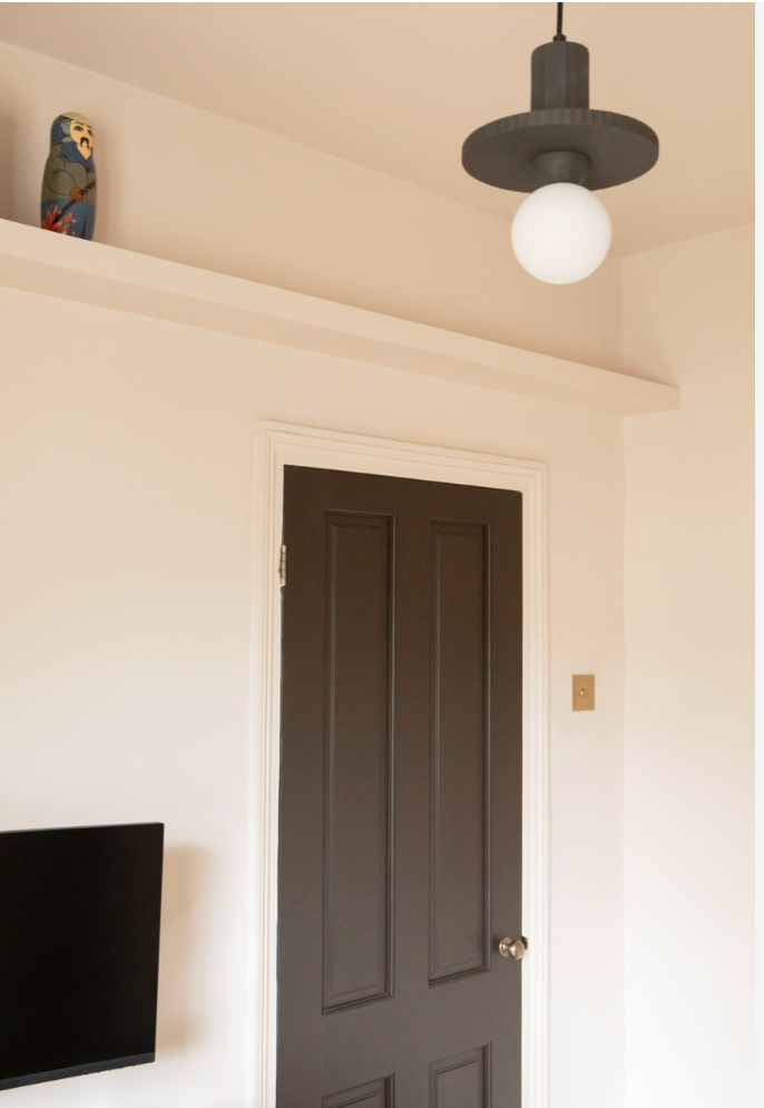 Claybrook  paints  on walls with brown paneled door, ceiling light fixture, and decorative object on a high shelf.