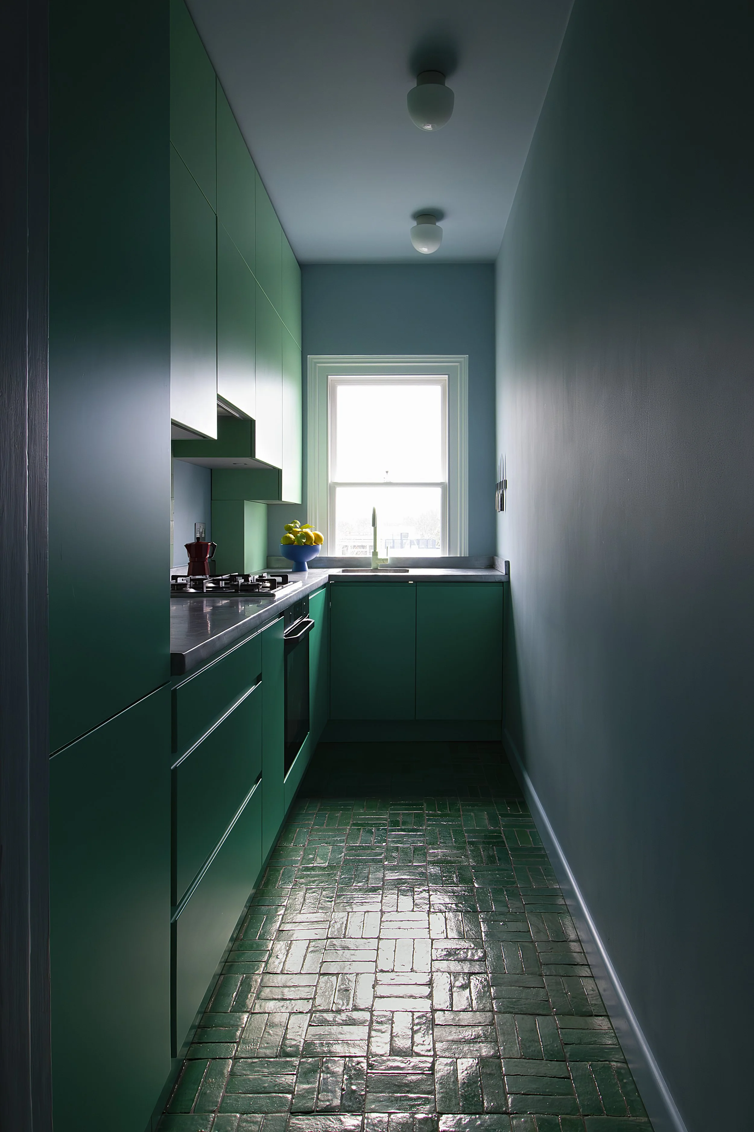 A narrow kitchen with green cabinets, a window, and a tiled floor.