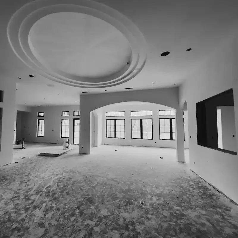 Interior view of a large, unfinished room with multiple windows, a circular ceiling design, and a rough floor, indicating ongoing construction.
