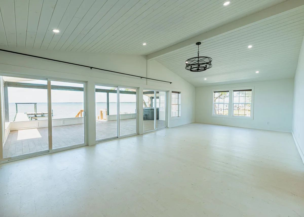 View from living room space out multiple sliding glass doors to the Pensacola bay, white floors, walls and ceilings and black accents