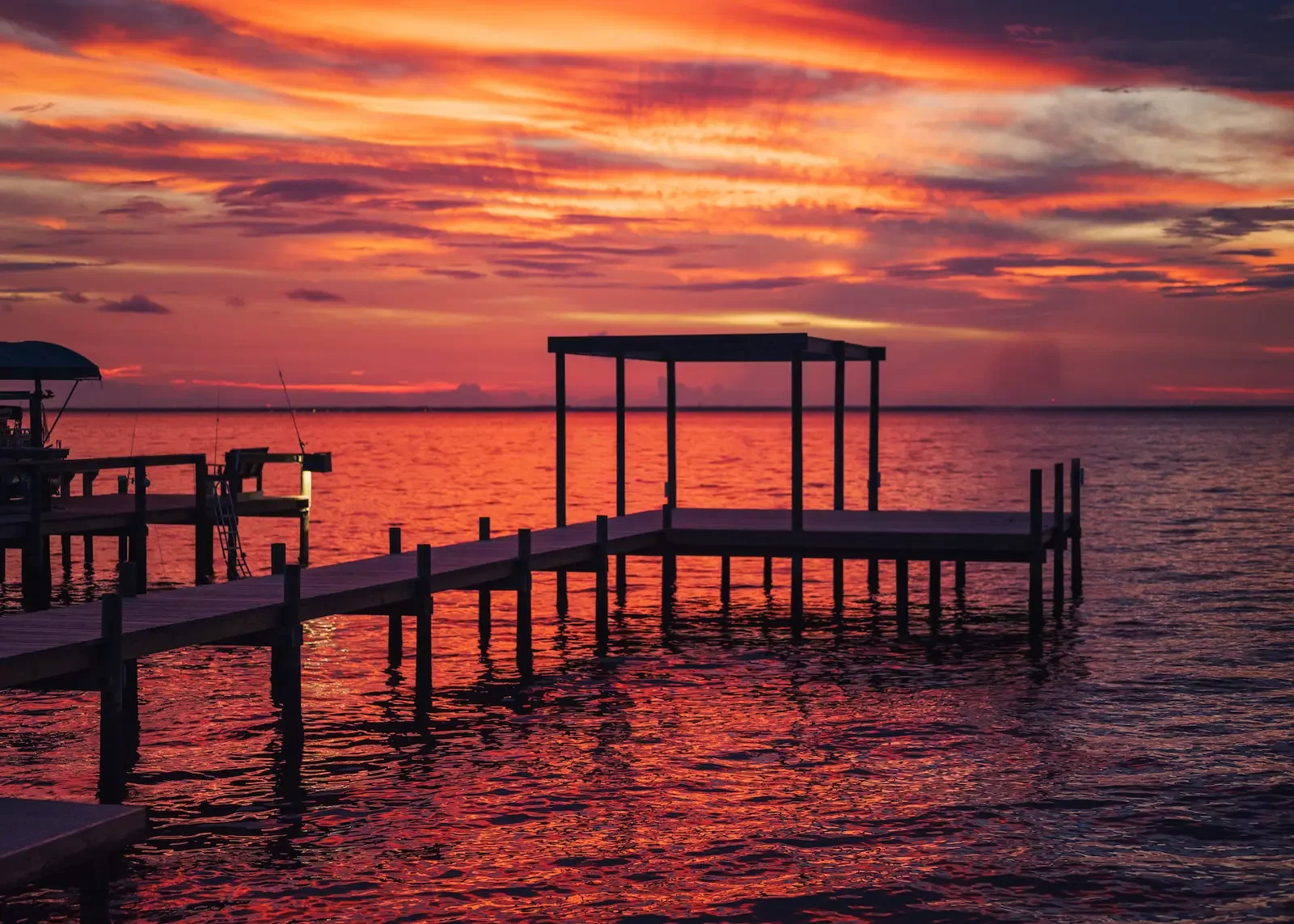 A dock extending into a calm body of water during a vibrant sunset with colorful sky and reflections on the water