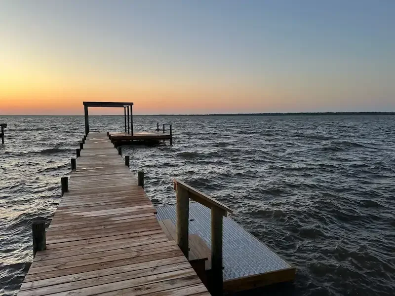 Wooden dock extending into a body of water during sunset, with a covered structure at the end of the dock.