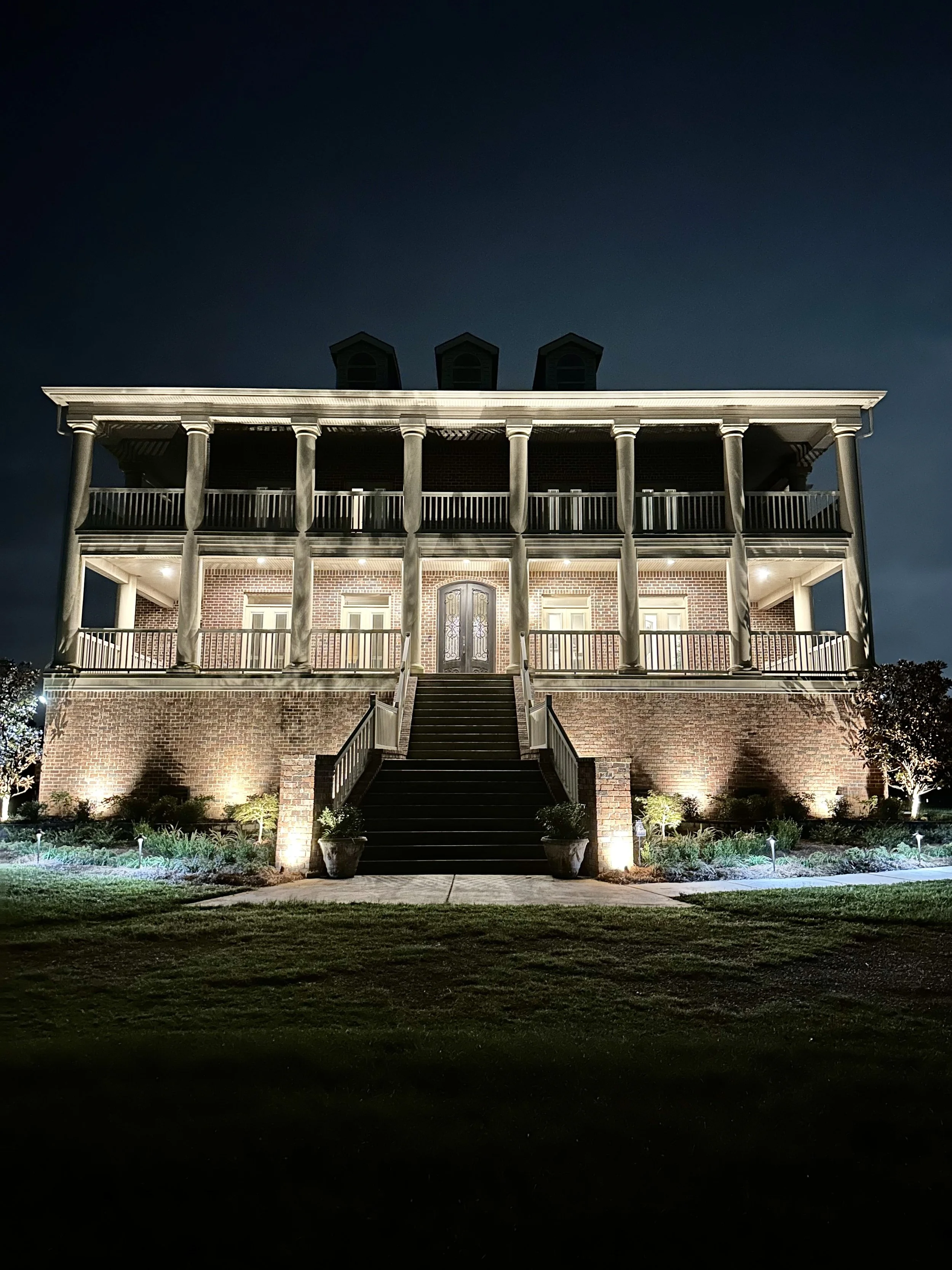 Grand Gulf Coast home entrance illuminated by landscape lighting, highlighting architectural details and front steps.