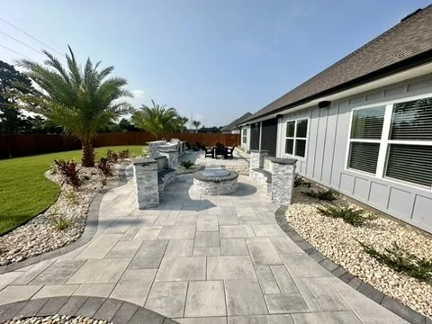 Expansive stone patio with lush landscaping, fire pit, and palm trees.