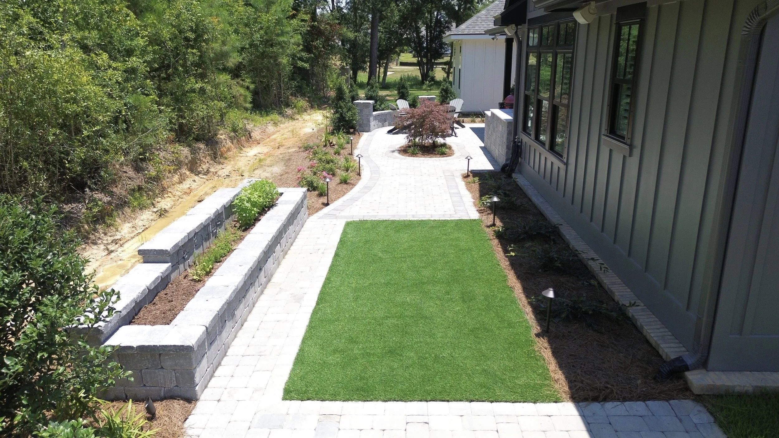 Beautiful Gulf Coast backyard with artificial turf, paver walkway, and landscaped retaining wall, creating a functional and low-maintenance outdoor space.