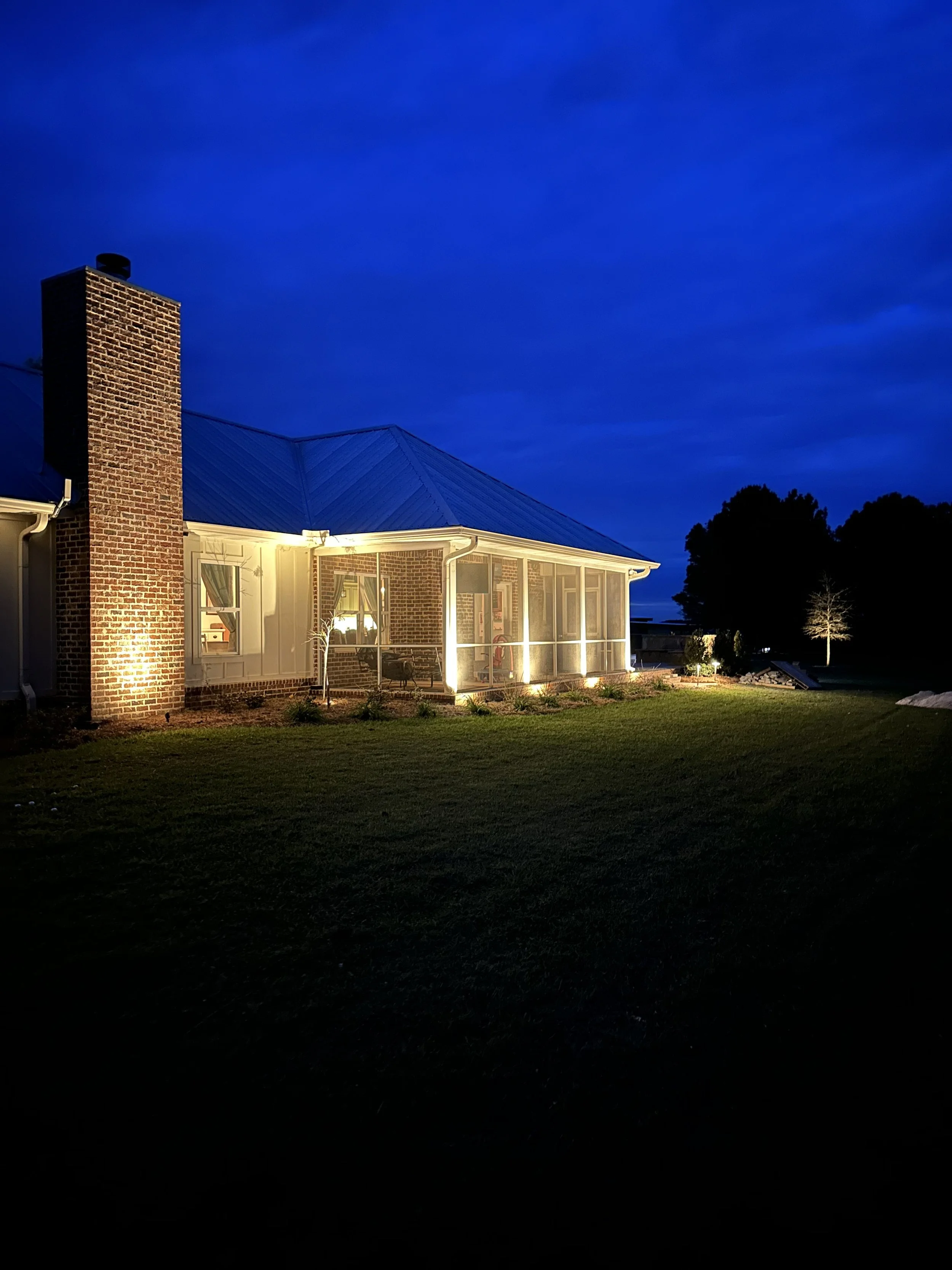 Elegant colonial home with landscape lighting highlighting its brick exterior and manicured garden in a Gulf Coast setting.