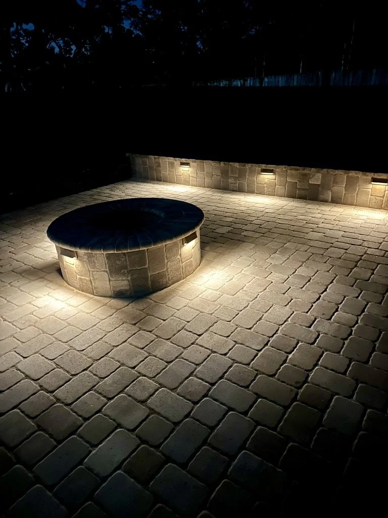  Illuminated circular fire pit surrounded by neatly arranged stone pavers.