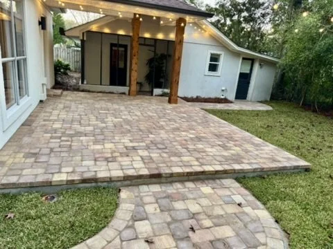 Cozy outdoor patio with charming paver paths, lush grass, and string lighting.