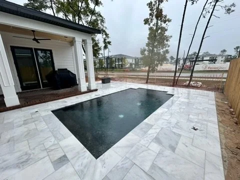 Luxury pool with marble pavers, showcasing modern design and sophisticated backyard aesthetics.