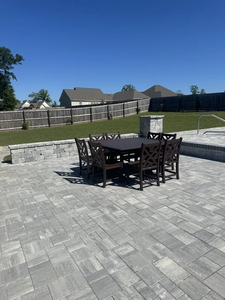 Large outdoor dining area with paver flooring, surrounded by modern and clean landscaping.