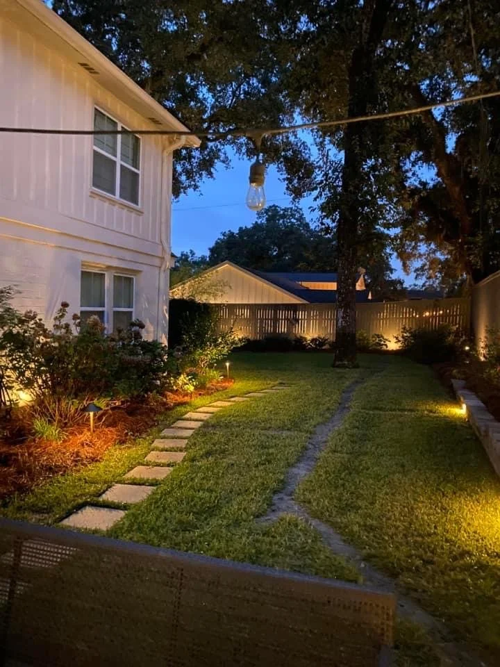 Backyard pathway with landscape lighting illuminating plants and walkways for evening ambiance and safety.