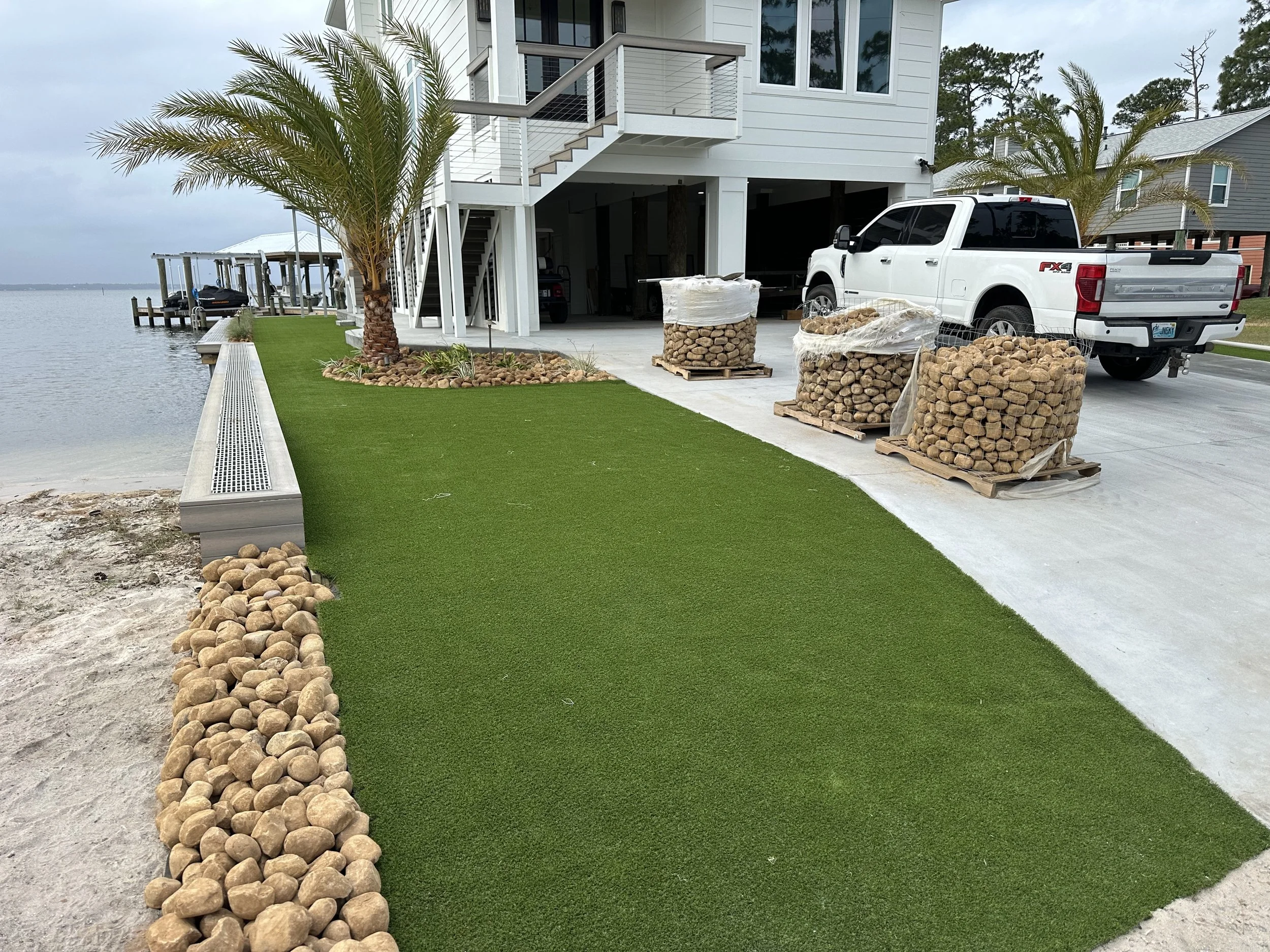 Waterfront Gulf Coast home with artificial turf, palm trees, and rock landscaping, creating a low-maintenance, coastal outdoor space.