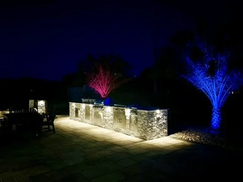 Night-lit backyard kitchen featuring colored lighting and luxurious stone accents