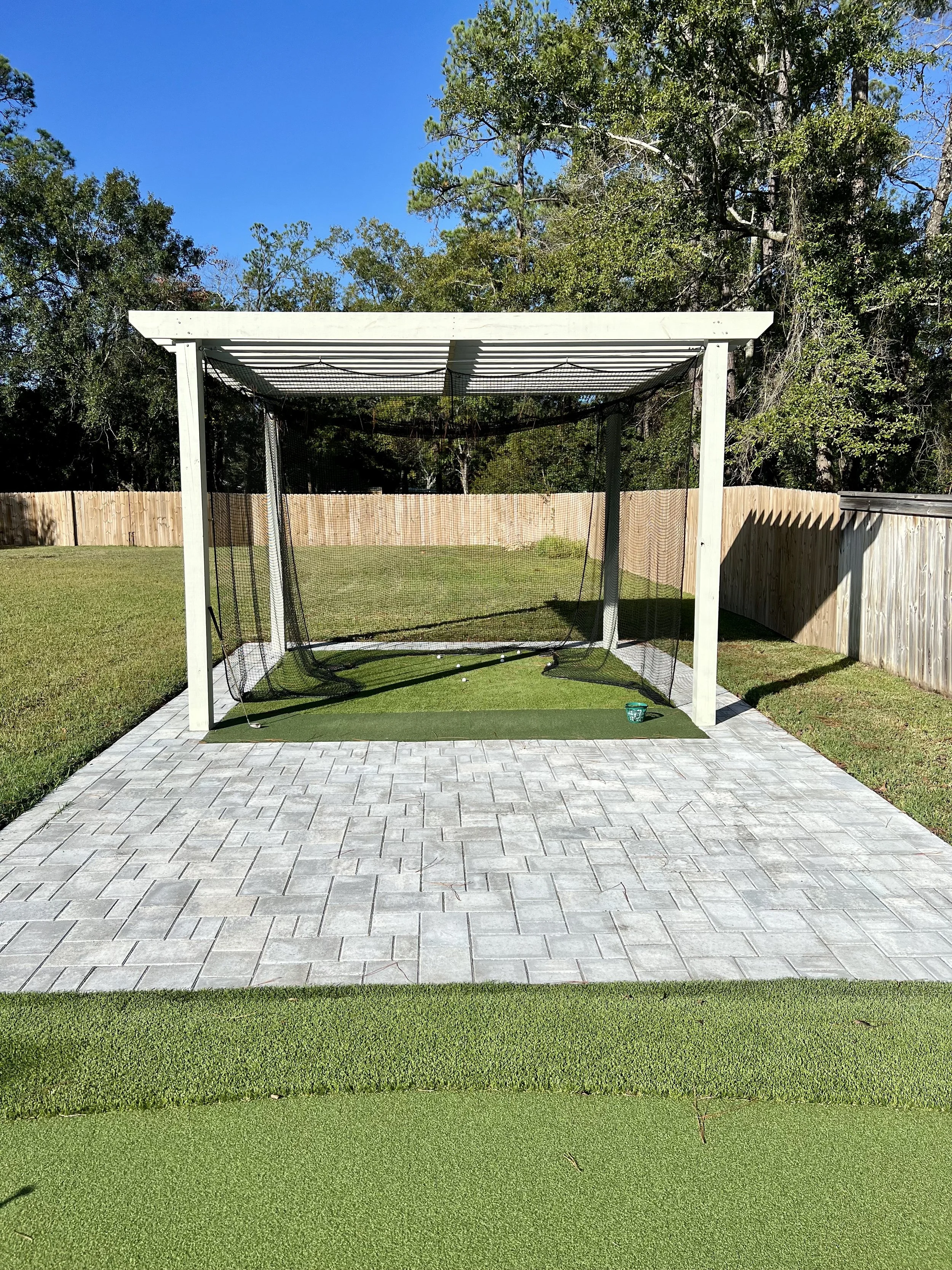 Backyard golf practice net on a paver patio with artificial turf in a Gulf Coast landscape, providing a dedicated training space.