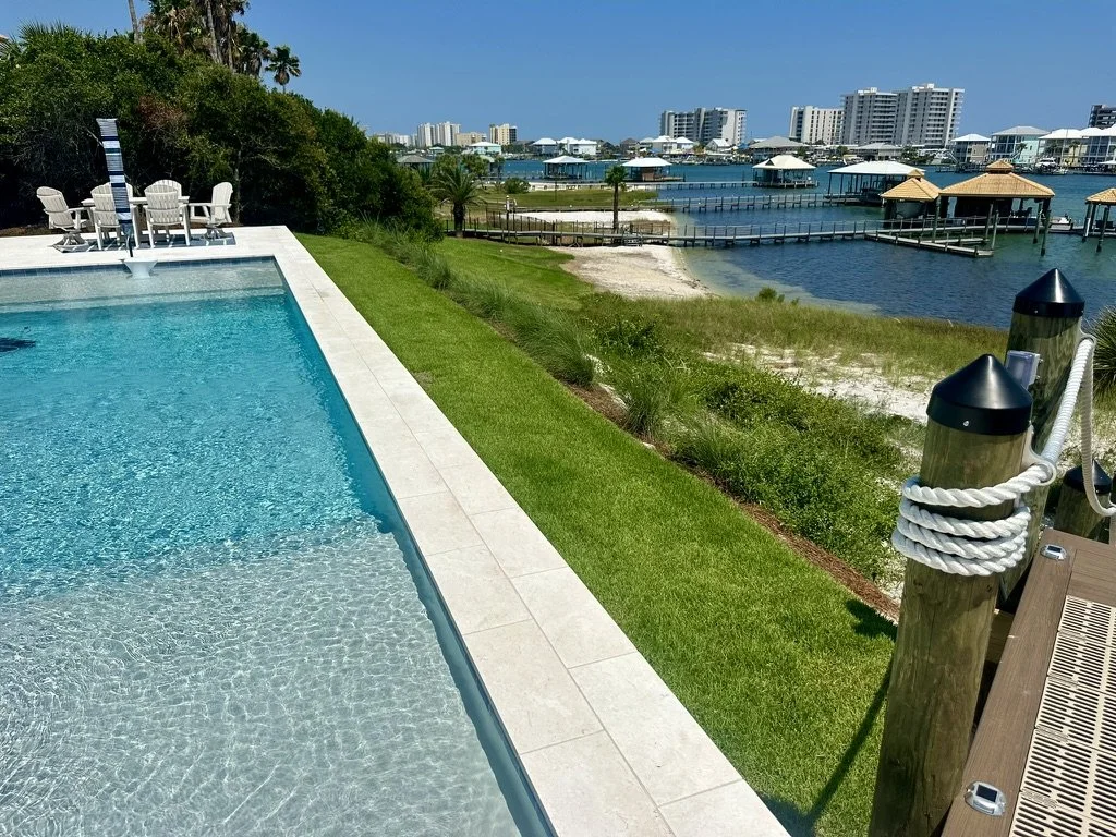 Luxury waterfront landscaping with a pristine pool, lush grass, and serene views.
