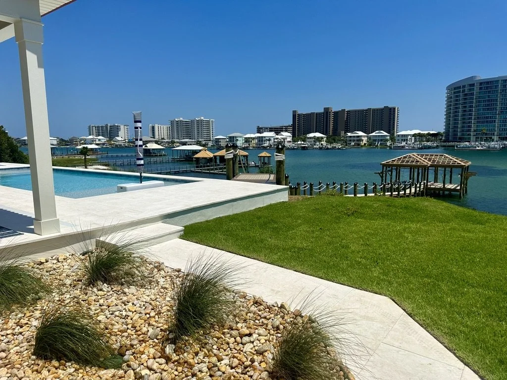 Elegant waterfront backyard with lush grass, pebble designs, and stunning ocean views.