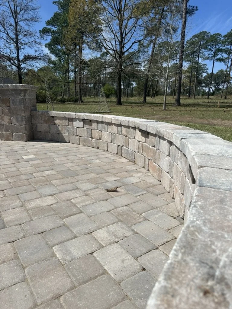 Outdoor stone patio with a curved retaining wall, surrounded by a natural wooded landscape, ideal for backyard landscaping and hardscaping projects