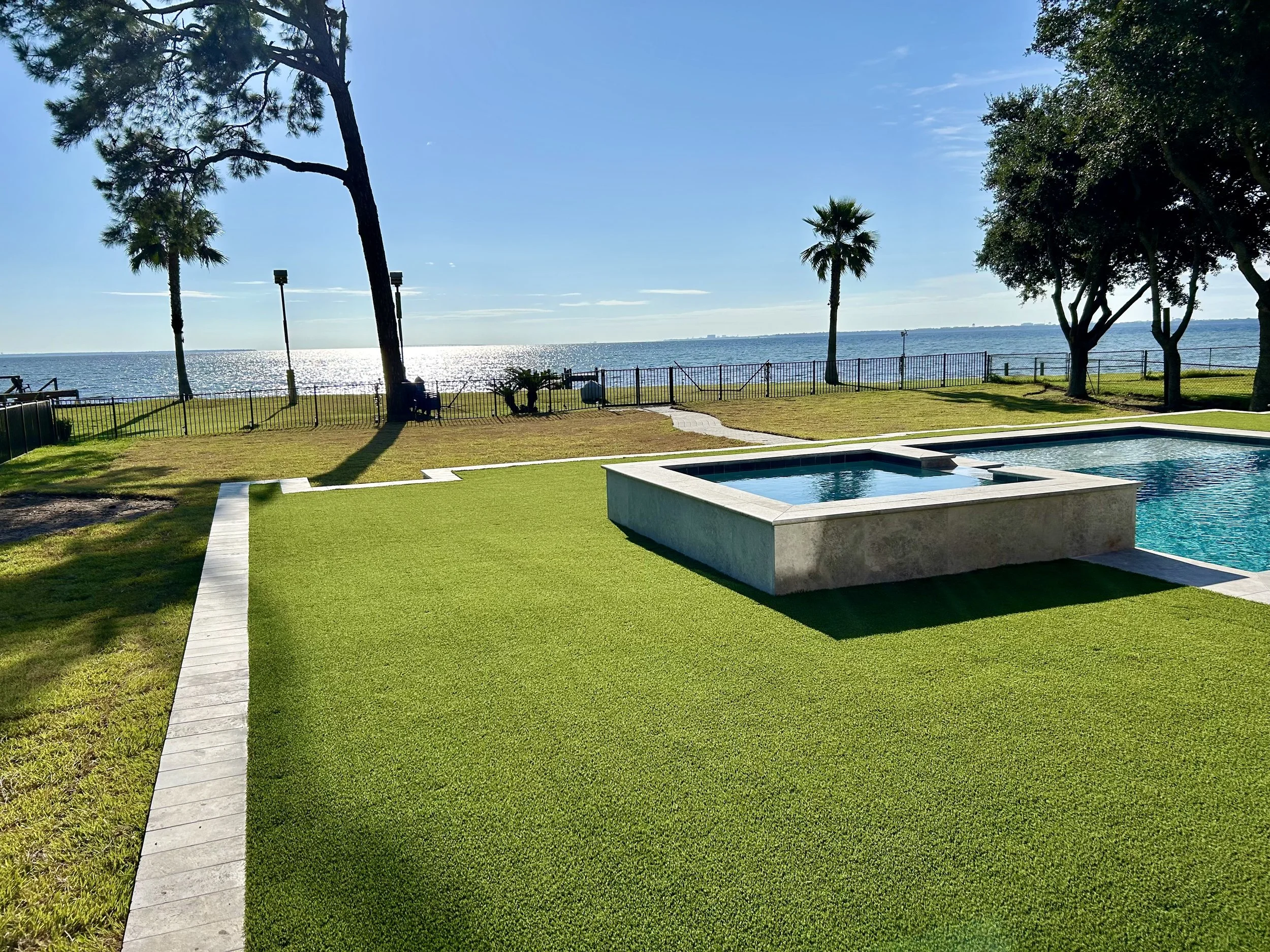 Stunning Gulf Coast waterfront backyard with artificial turf, modern pool, and spa overlooking the water, designed for luxury outdoor living.