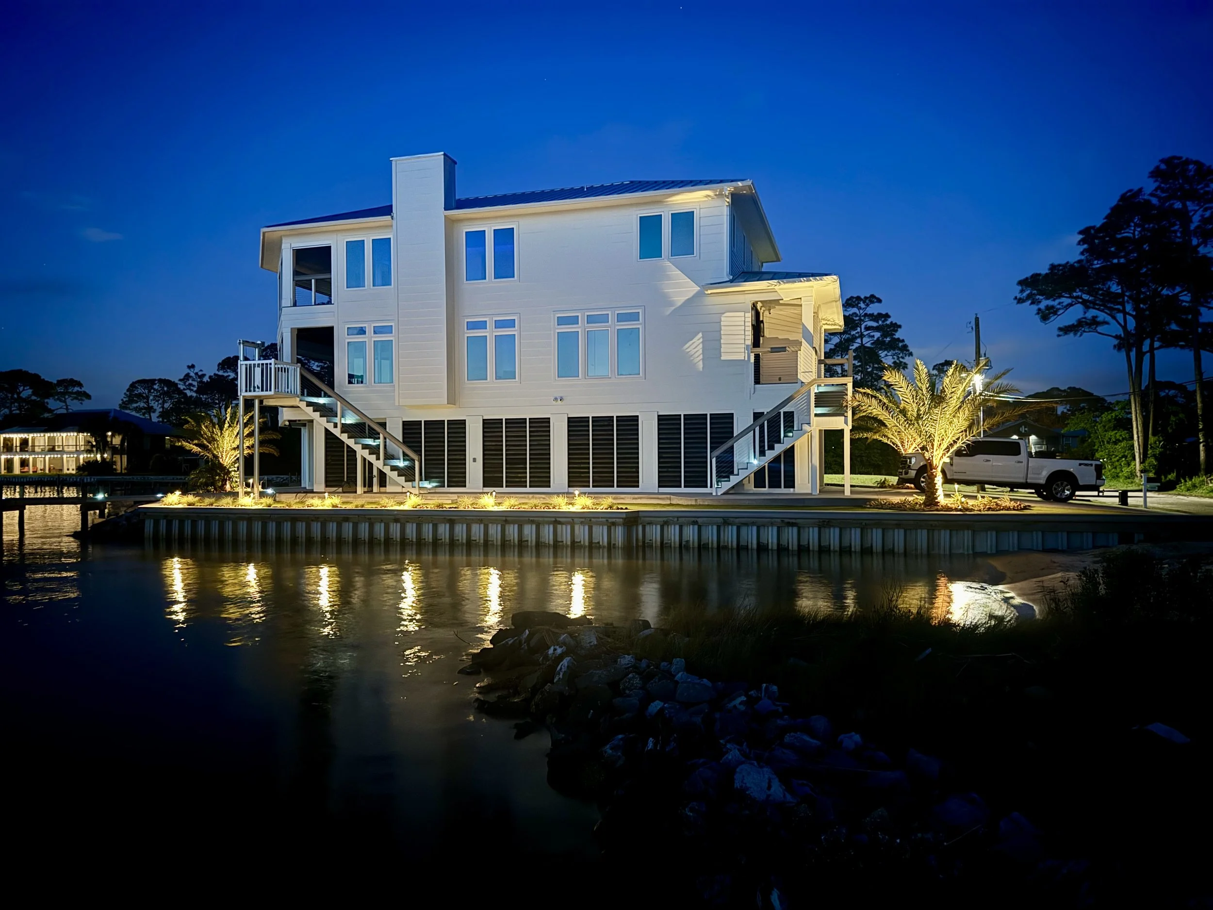 Coastal waterfront home with outdoor lighting showcasing architectural and landscape features along the Gulf Coast.