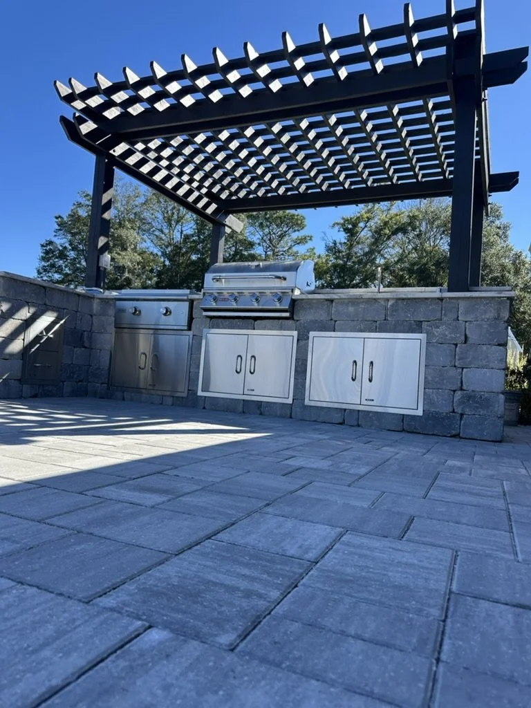 Sleek pergola-shaded outdoor kitchen with premium stone pavers and appliances.