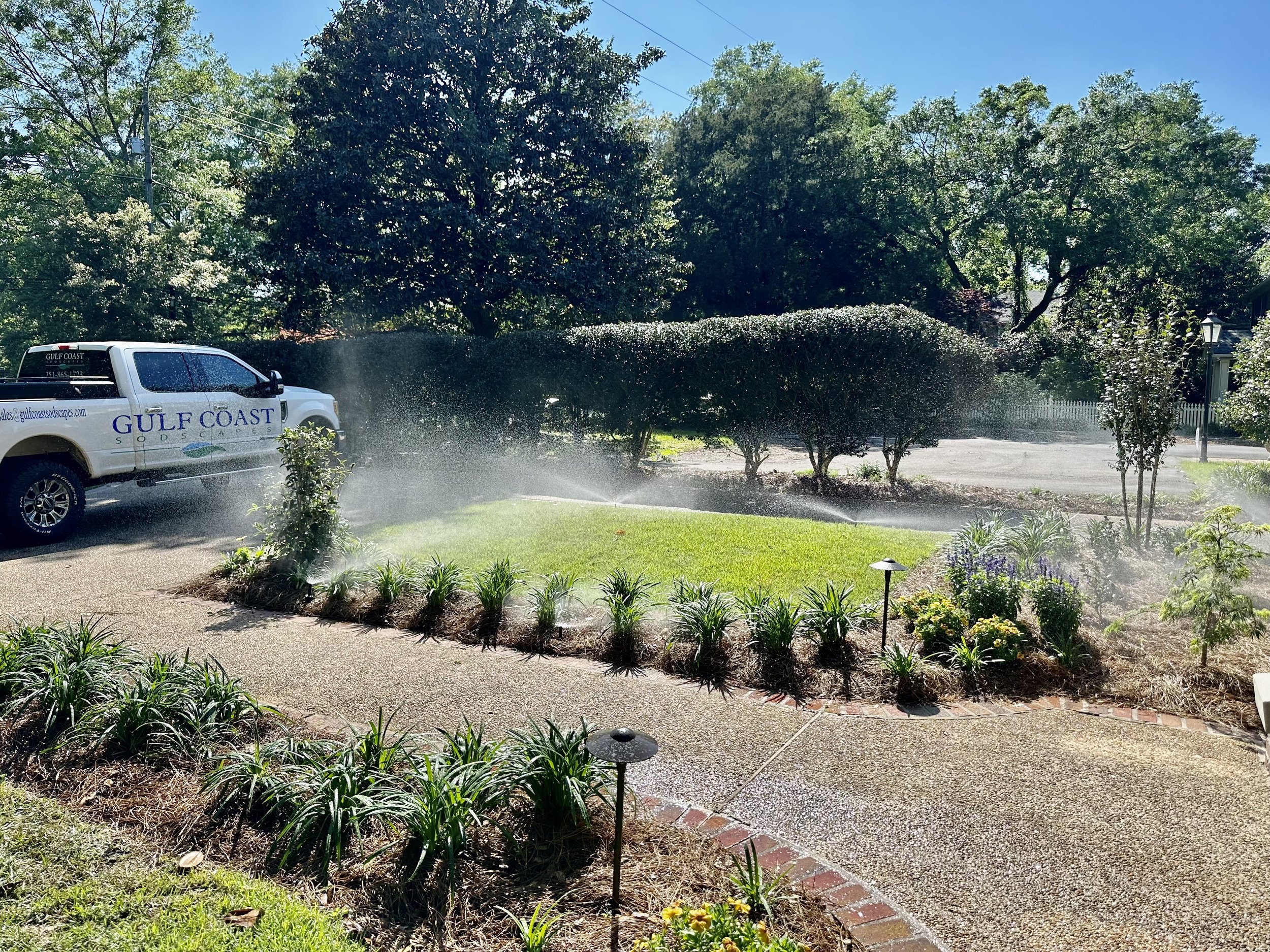 Gulf Coast Sodscapes truck parked near a lawn with an active irrigation system, ensuring vibrant landscapes.