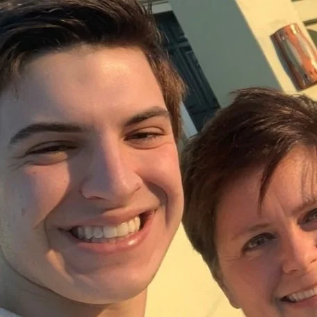 Close-up of a young man smiling next to an older woman, both outdoors.