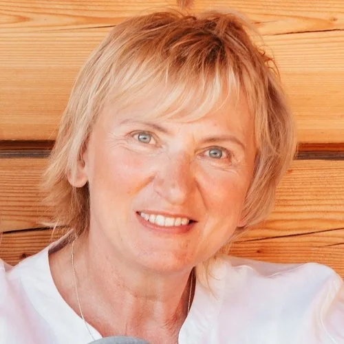 A woman with blonde hair smiling, sitting in front of a wooden wall.