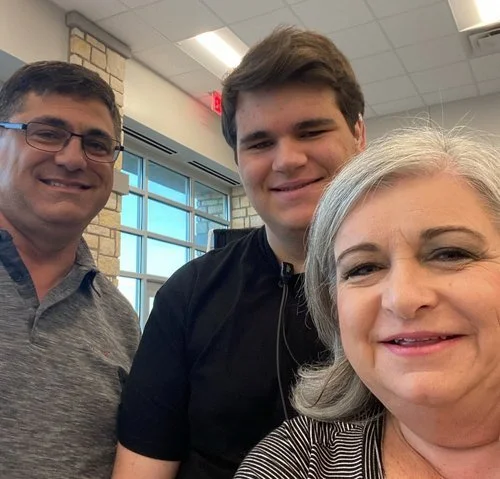 Three smiling people taking a selfie in a room with large windows and brick walls.