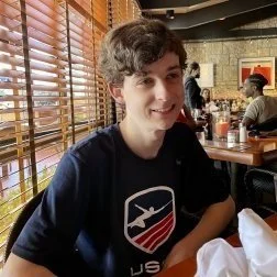 Young man with curly brown hair smiling at a restaurant table.