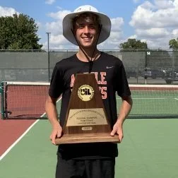 Person wearing a white wide-brimmed hat holding a gold tennis trophy on a tennis court.