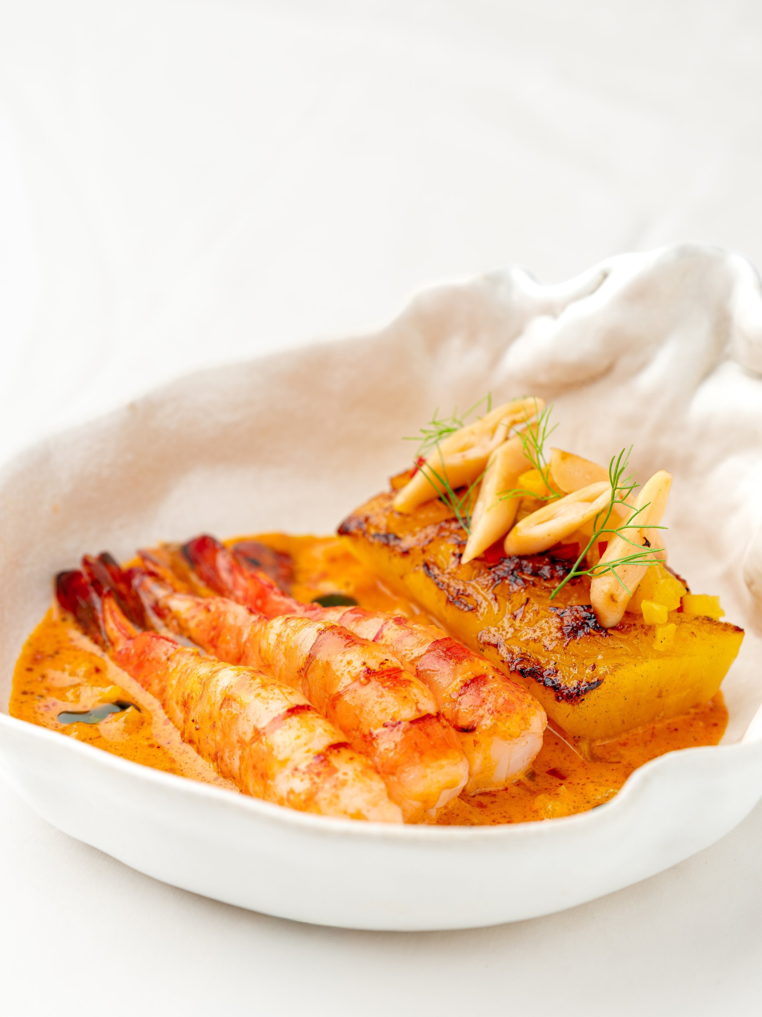 A seafood dish with grilled shrimp and grilled yellow fish topped with herbs, served with a creamy sauce in a white bowl.
