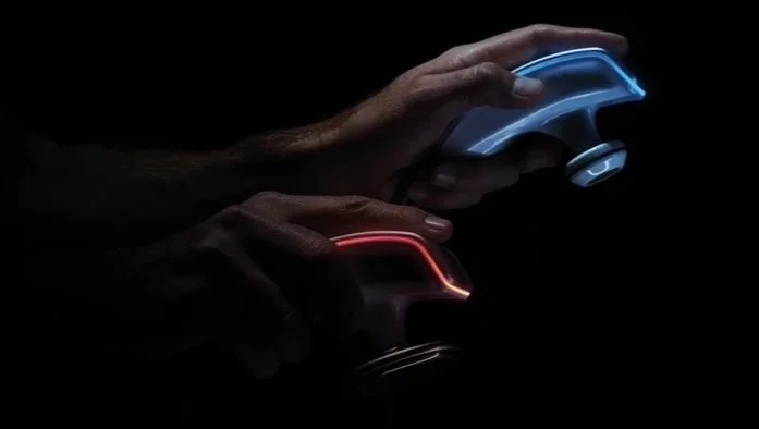 Two hands holding game controllers, one with blue lights and one with red lights, in a dark setting.