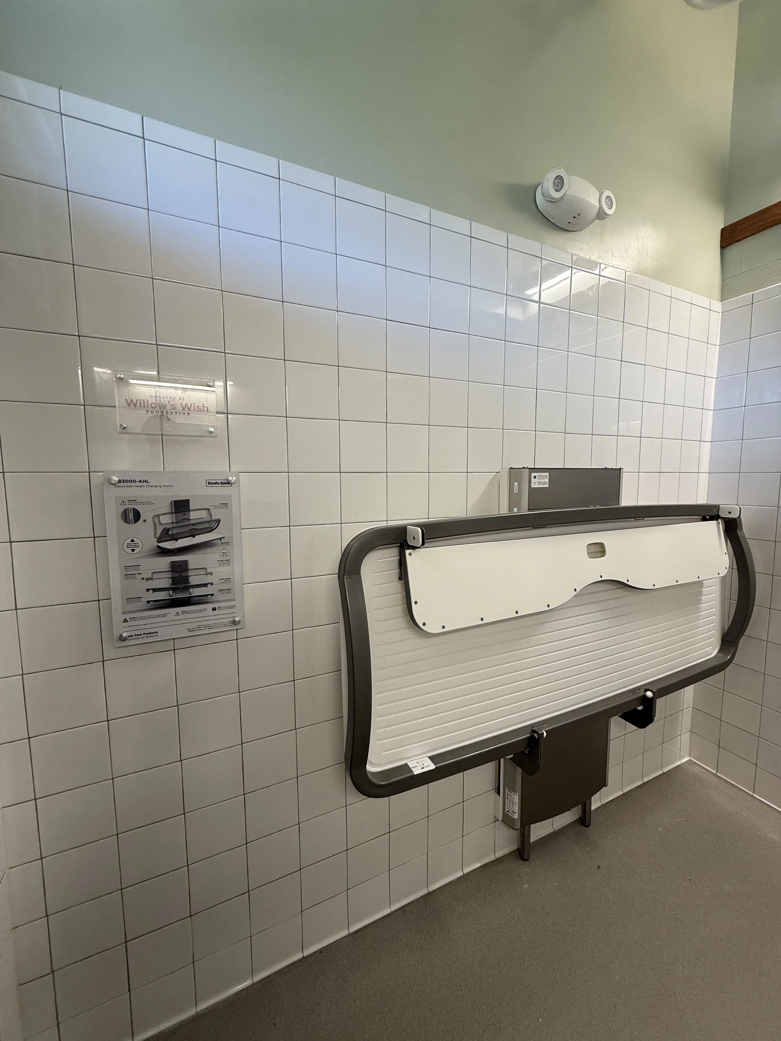 Inclusive changing table next to a Willow's Wish Foundation mounted sign.