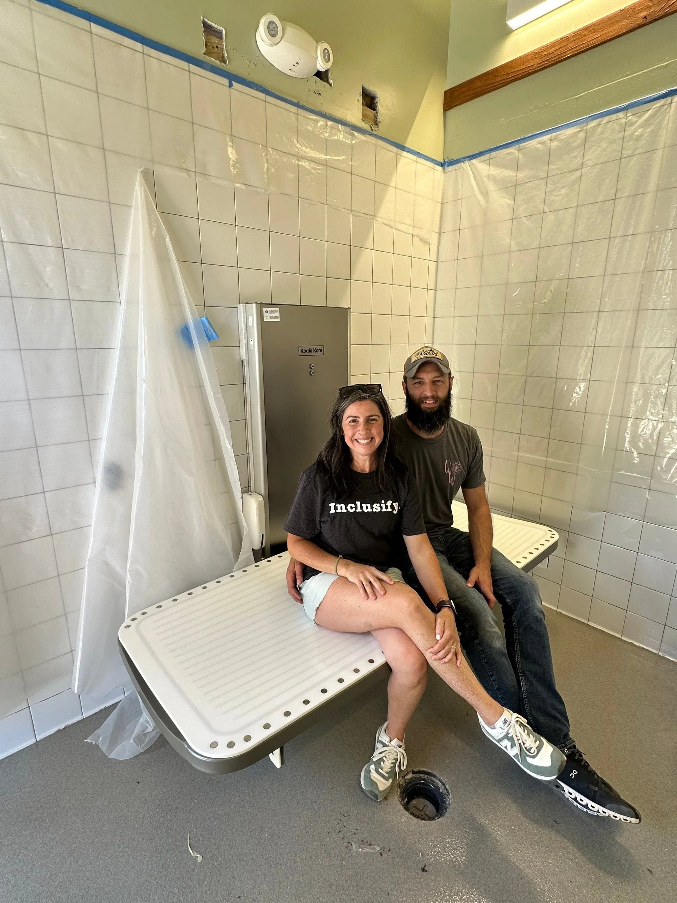 Mark and Erika Dail demonstrating the strength of a new powered changing table by both of them sitting on it. 