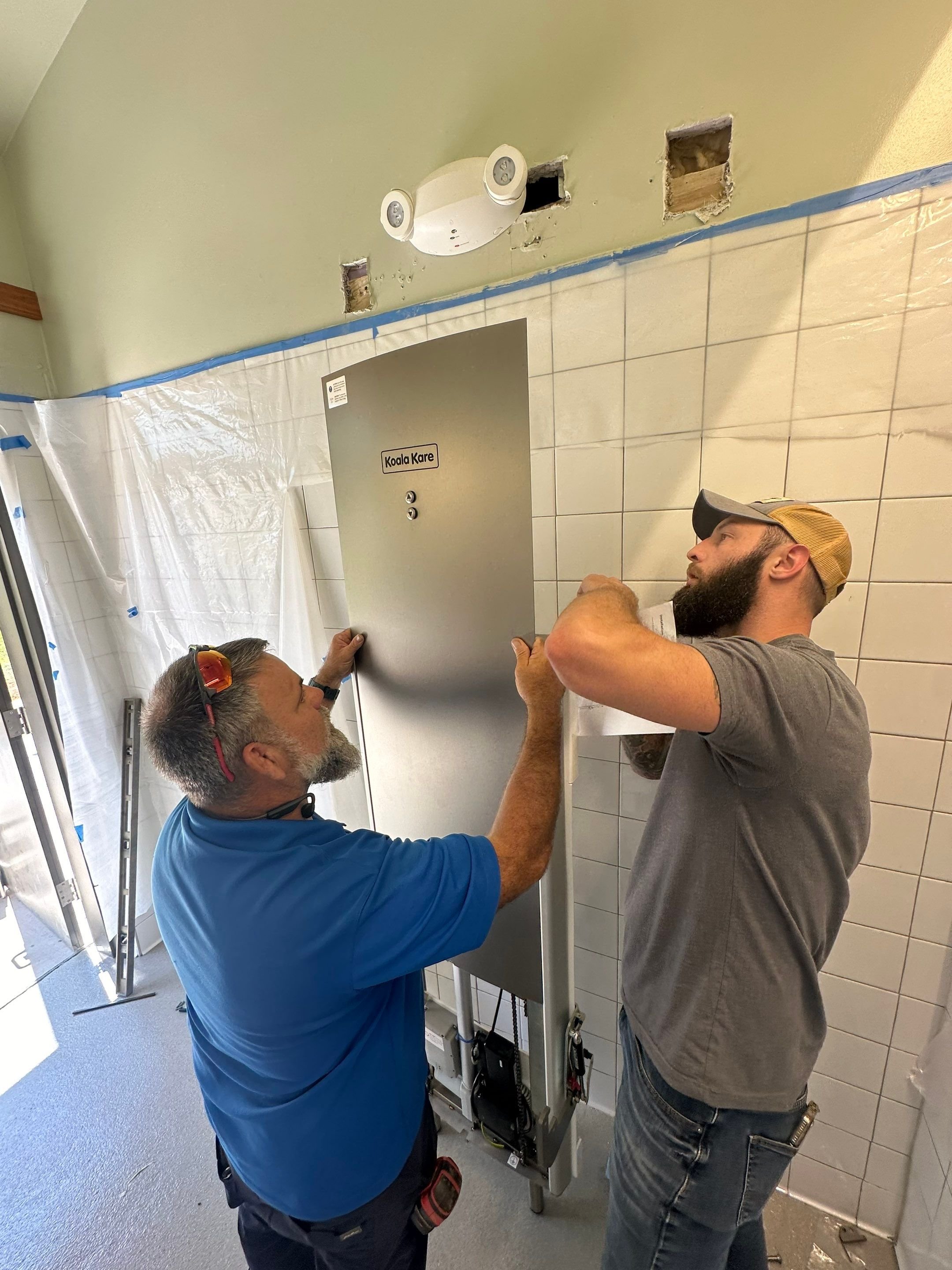 Mark Dail and a Willow's Warrior holding up and mounting an electronic changing table component. 