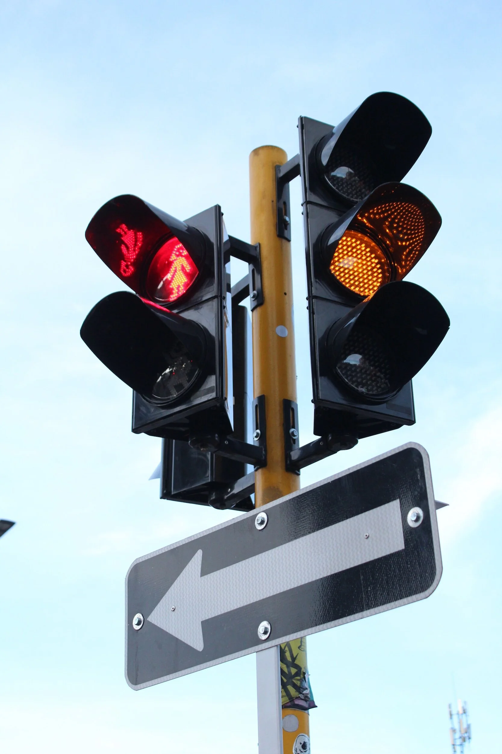 A traffic light with red, yellow, and green signals, with the red light illuminated and a pedestrian walking sign. There is a black and white arrow sign pointing left.