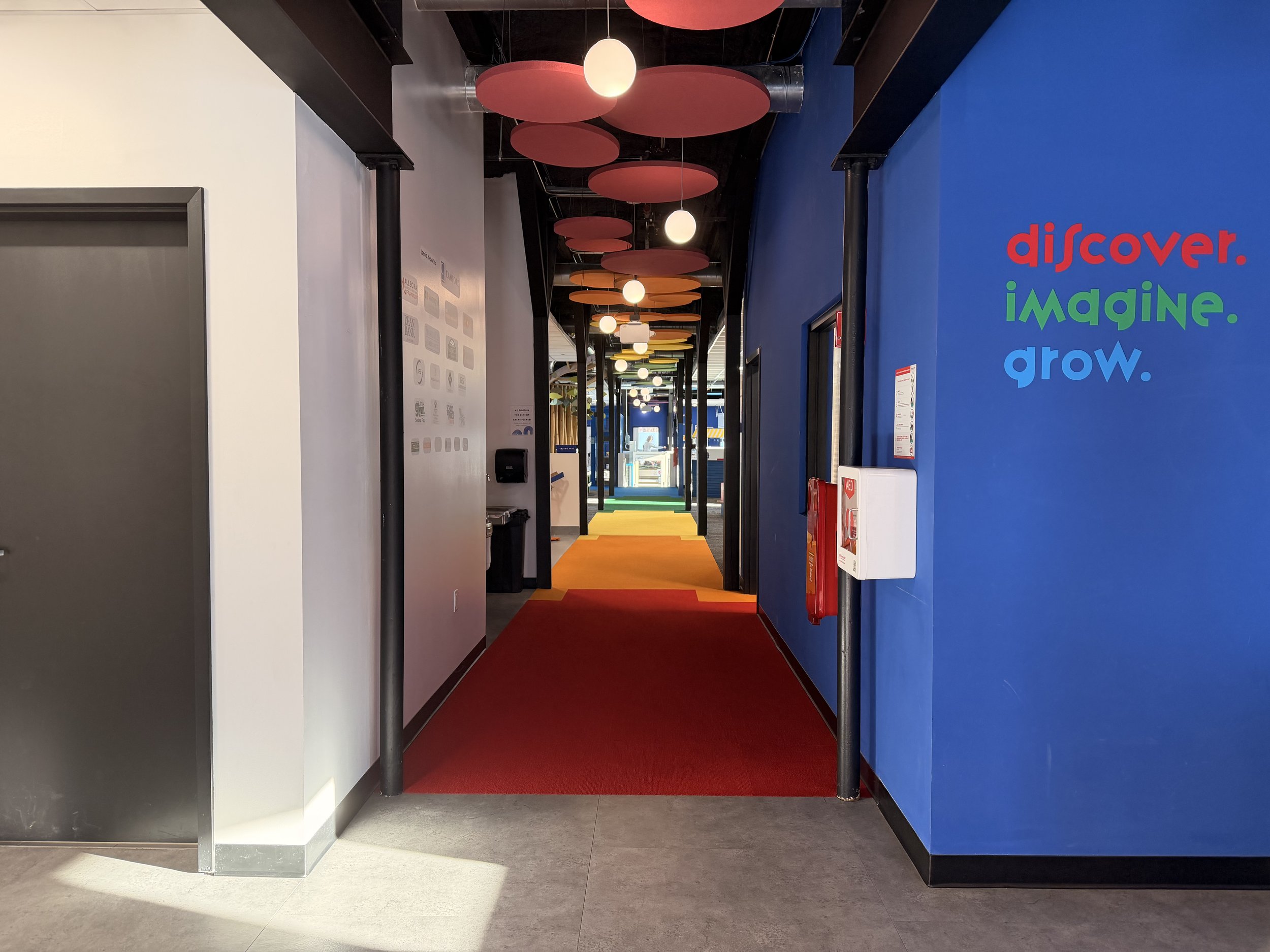 View into exhibits. Brightly colored ceiling tiles and carpeting.