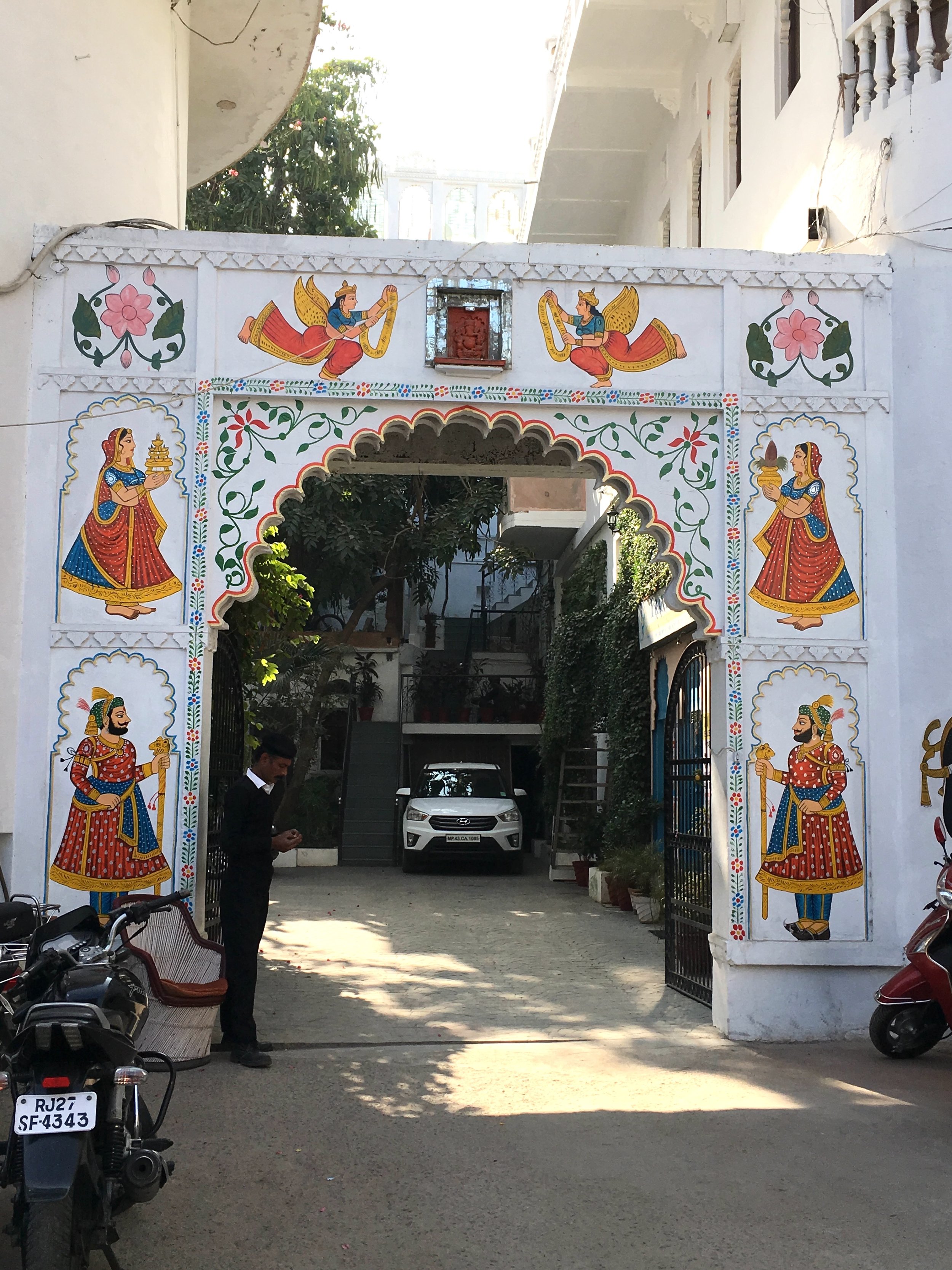 A gateway in Udaipur, India, with auspicious motifs, including a woman with the purnaghata, a full vessel, including water and vegetation like mango leaves and a coconut. The full vessel is a symbol of Lakshmi as she is also the source of all life.