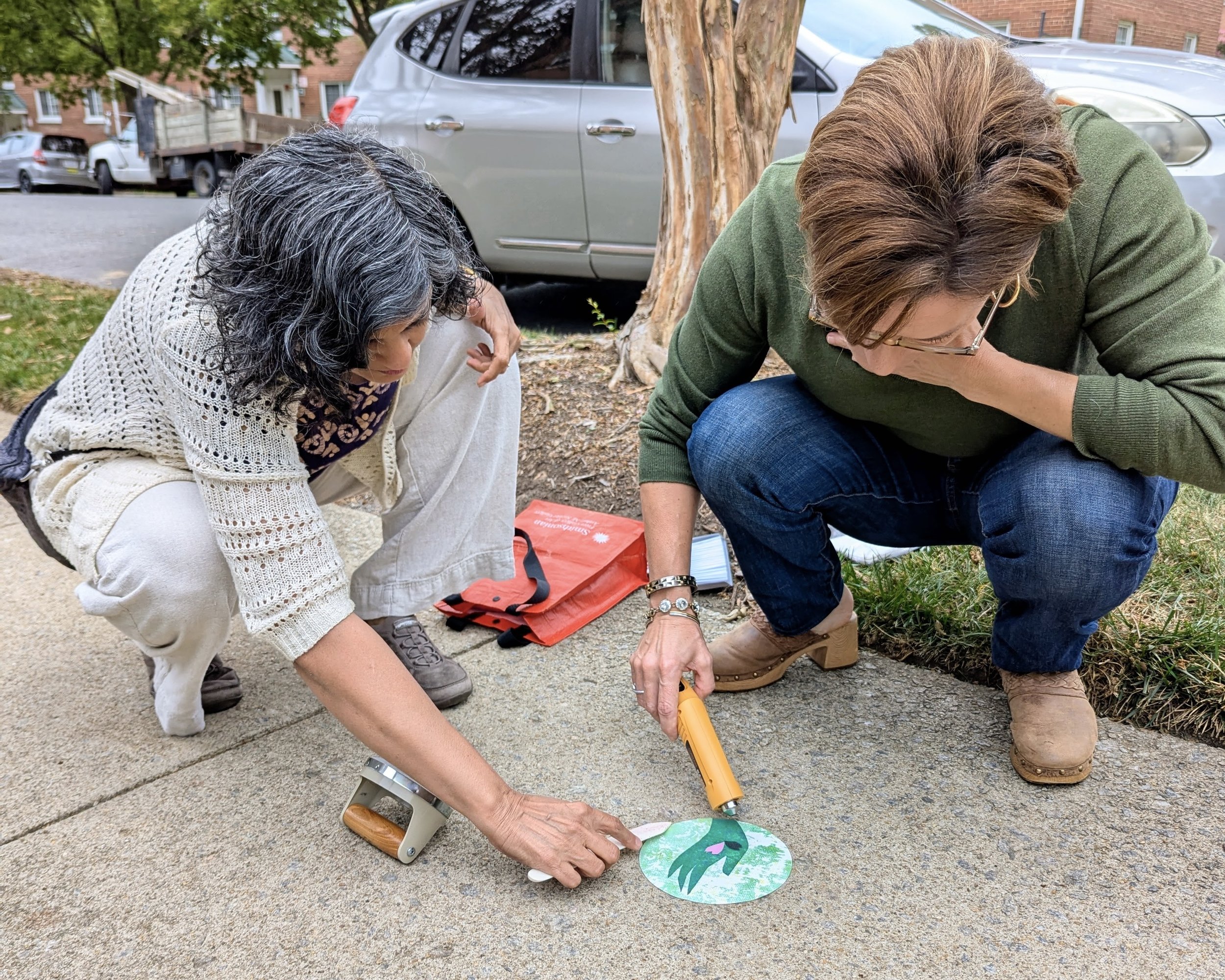 Ashley (right) and Sush put down a Stumbling Sticker on the sidewalk in Arlington from where neighbors were taken.