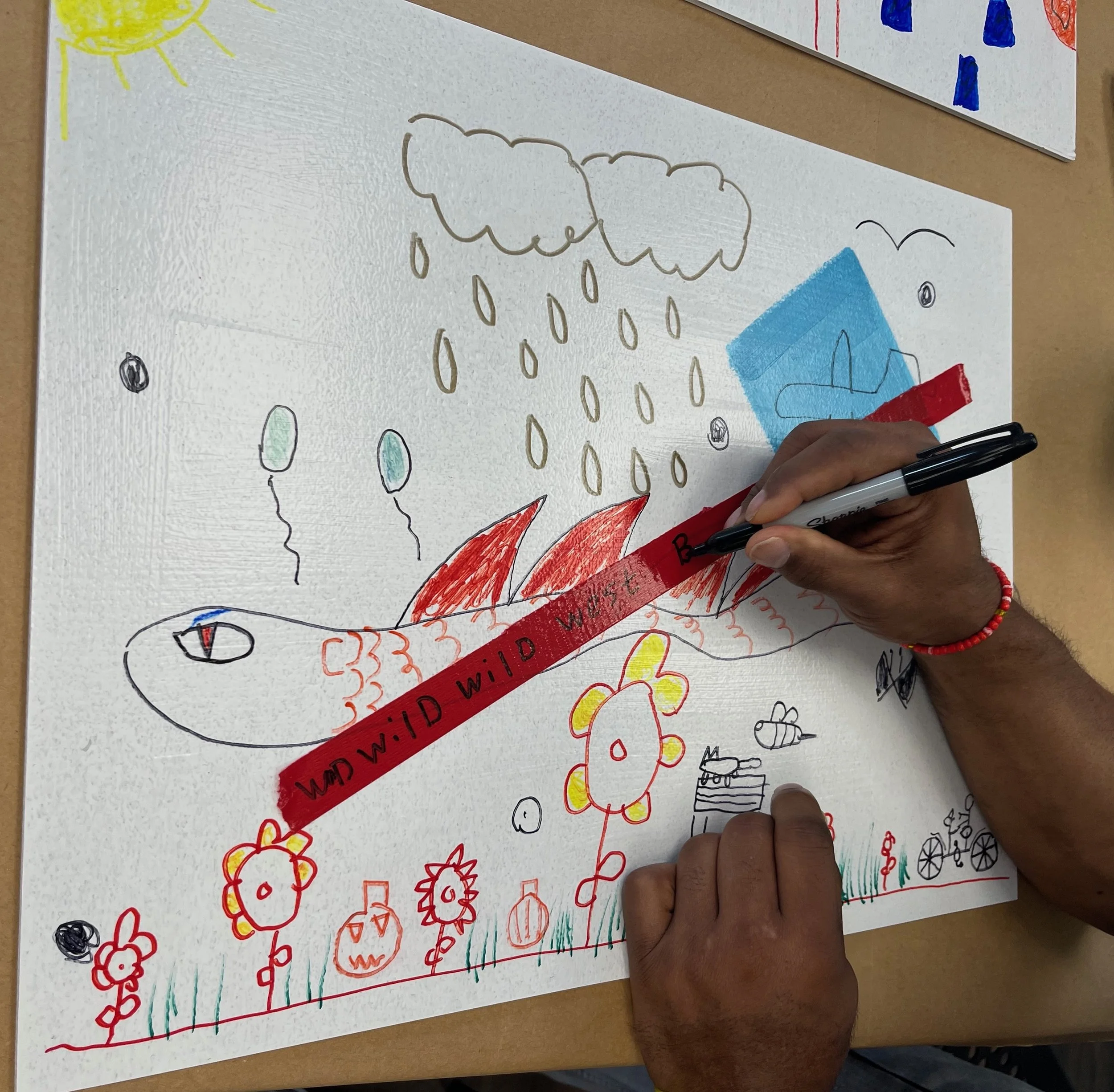A participant of AWE uses prompts given by the children to draw flowers and a dragon. He then added the red tape and put the lyrics of his favorite song on it, which we played as he made his artwork.