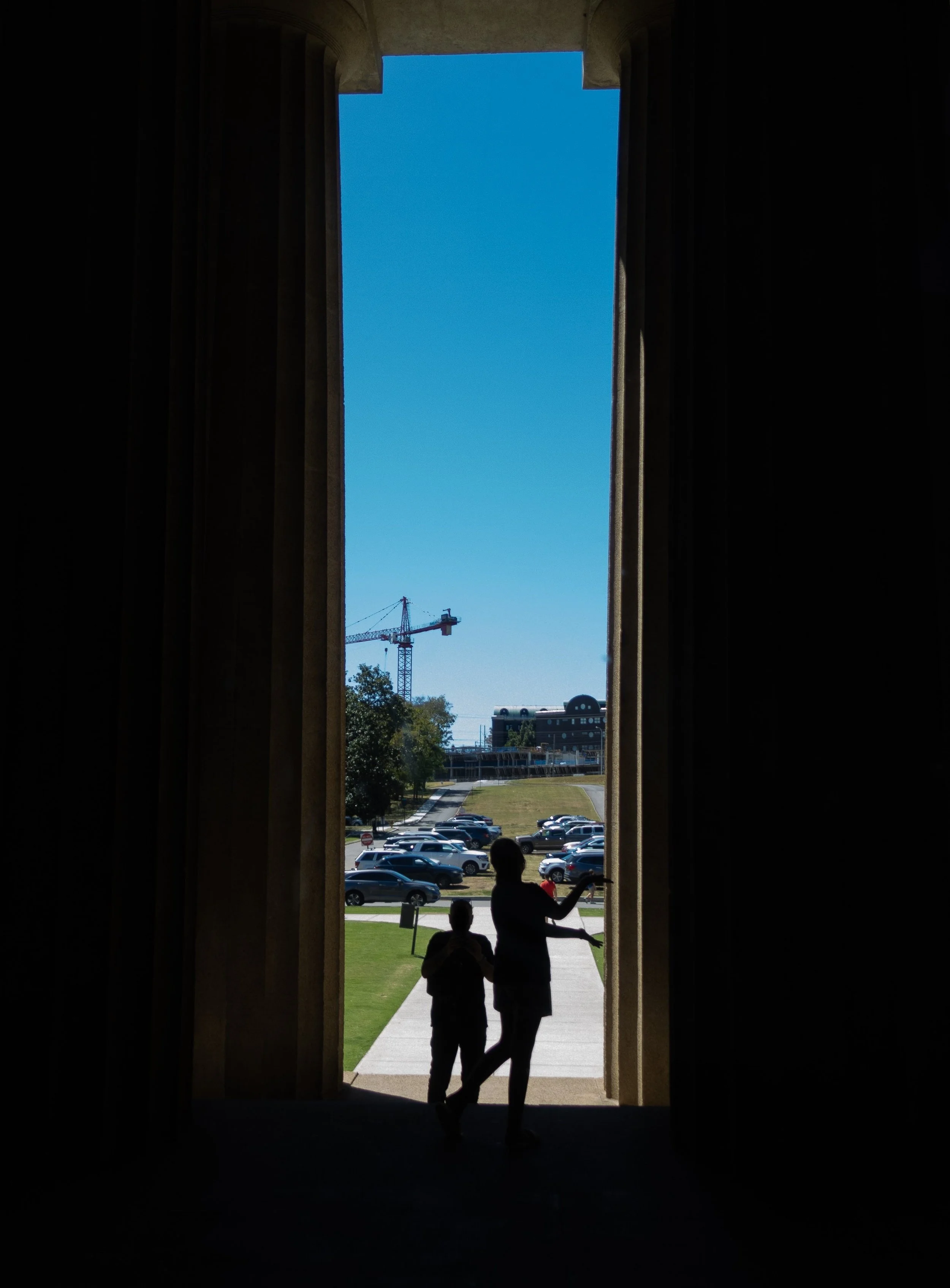 A little girl poses in front of a pillar outside the Parthenon while her father takes a picture