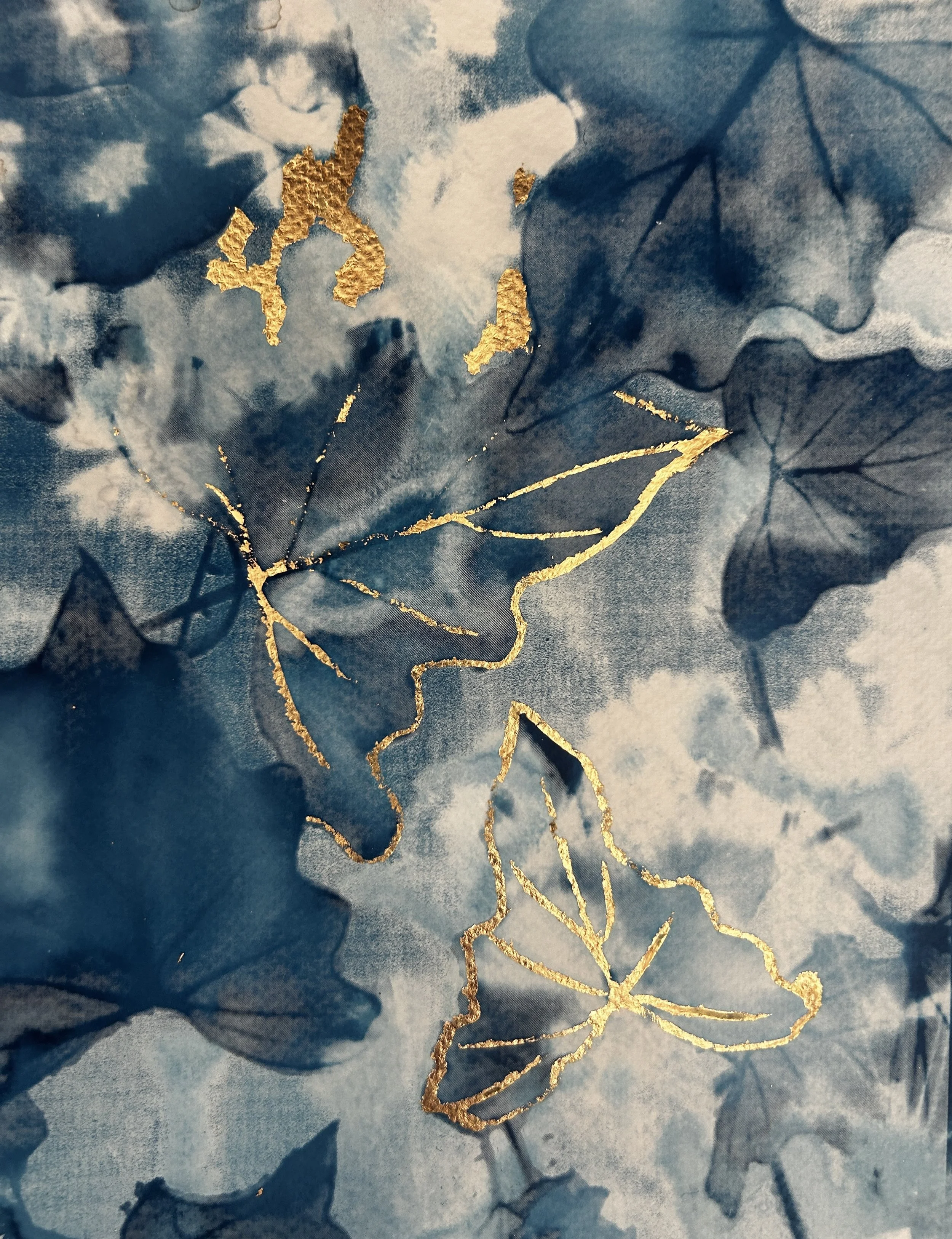 Close-up of a textured cyanotype paper with gold foil accents and dried leaves.