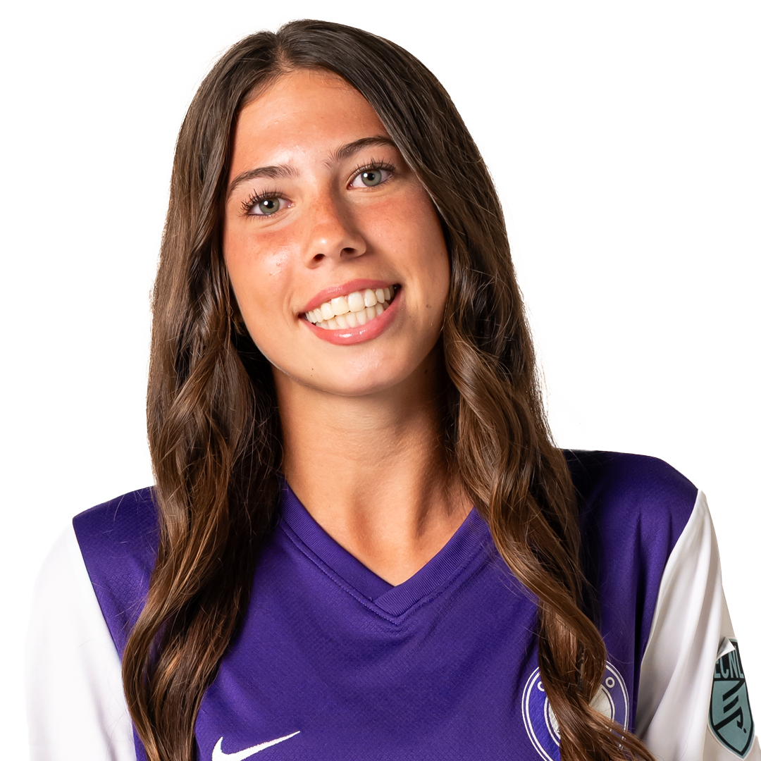 A smiling woman with long wavy brown hair, wearing a purple and white sports jersey with a logo on the chest and patch on the sleeve, against a plain white background.