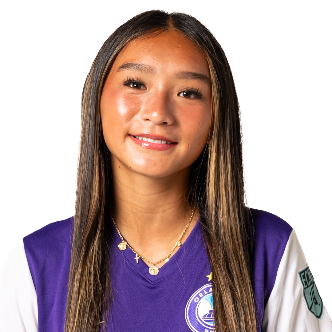 Young woman with long brown hair smiling, wearing a purple sports jersey with Orlando Pride logo and gold jewelry.