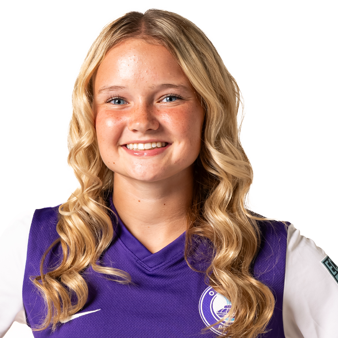 A young woman with long blonde curly hair, blue eyes, and freckles smiling, wearing a purple sports jersey with white and black details.