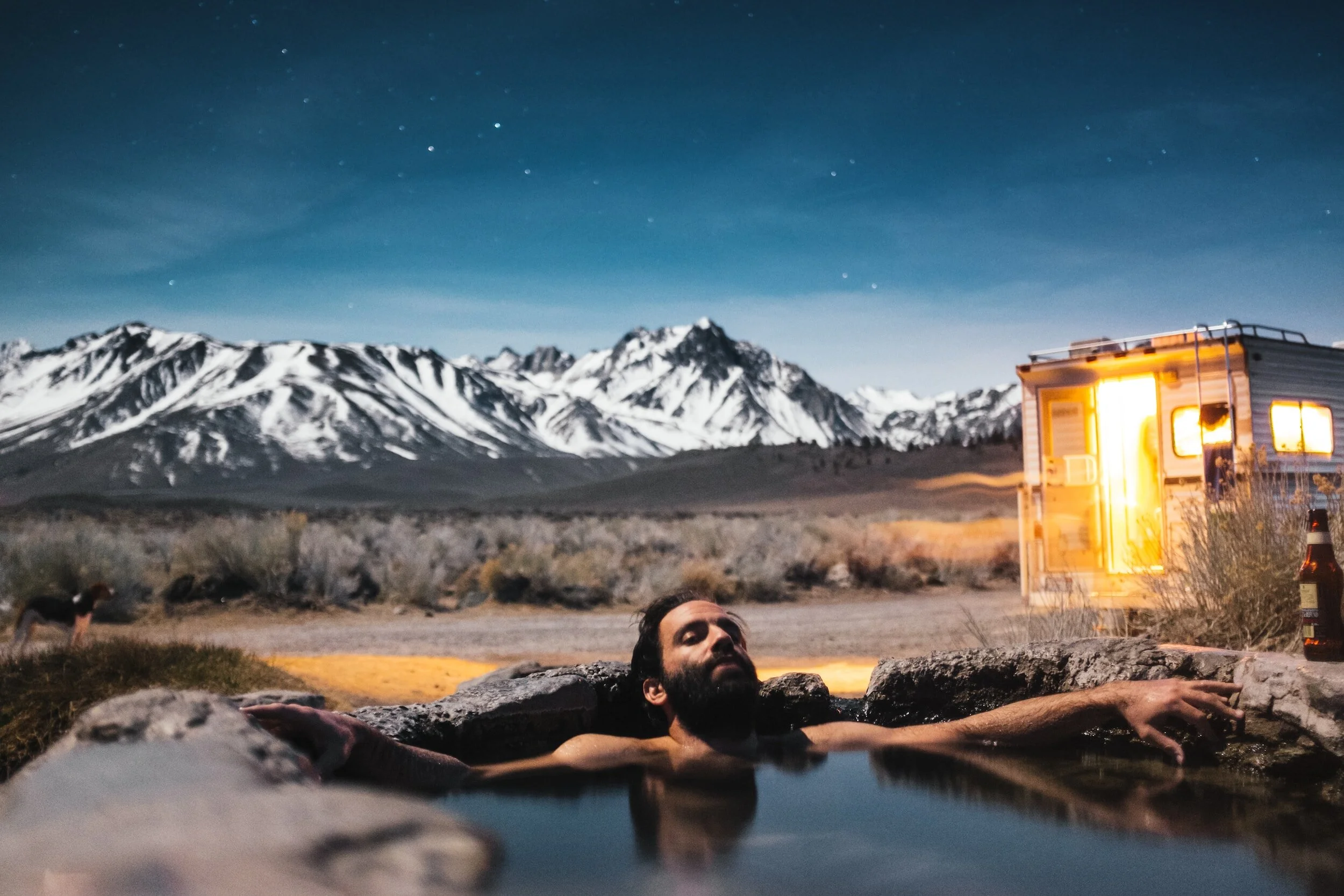 man in hot springs with snow capped mountains in distance