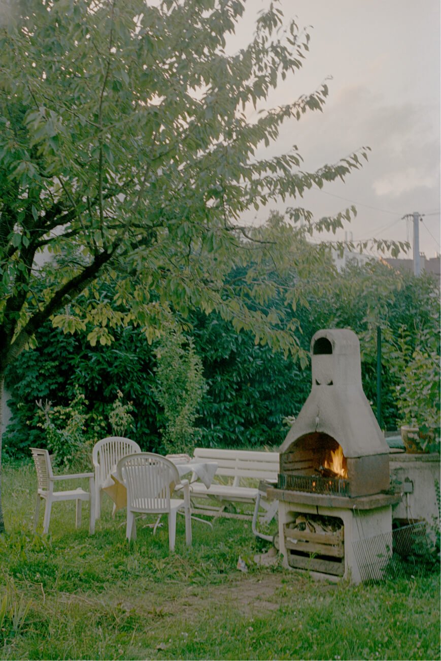 Un jardín vacío con sillas, bancos y una parrilla con las llamas encendidas.