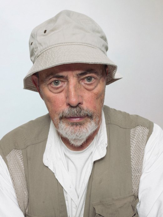 Retrato de Bruce Gilden usando chapéu contra um fundo neutro.