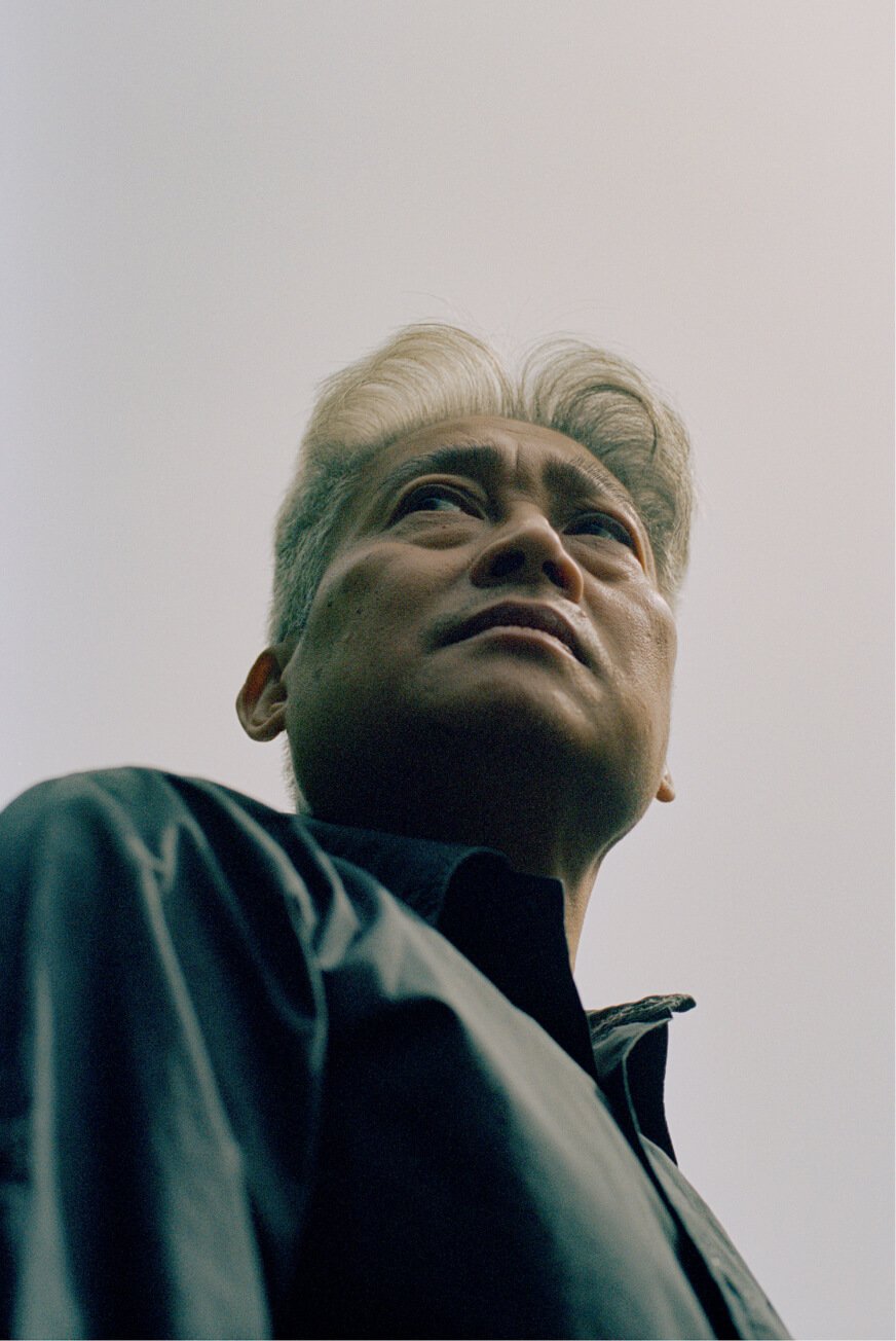 Un ritratto dal basso di un anziano uomo asiatico con una straordinaria capigliatura argentata.