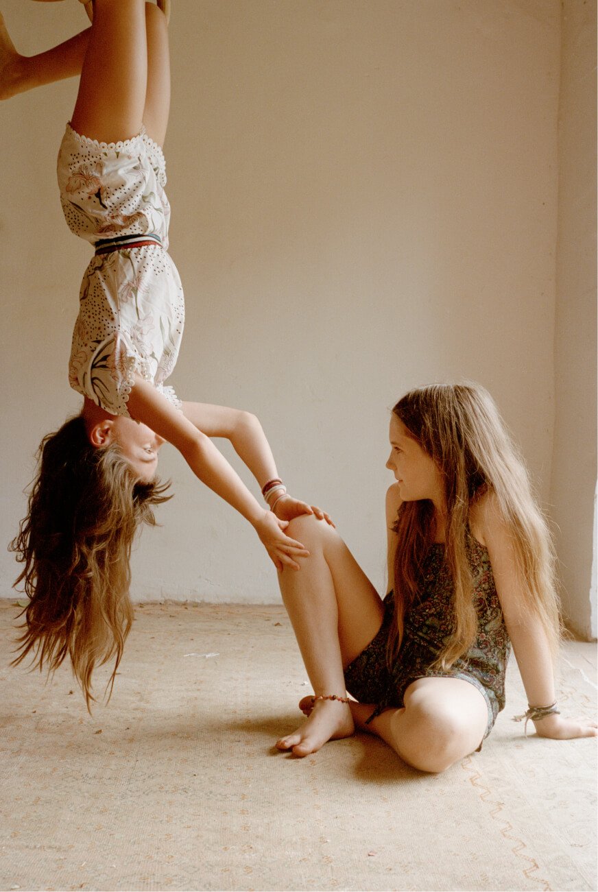 Kinder spielen mit einem jungen Mädchen, das kopfüber hängt.